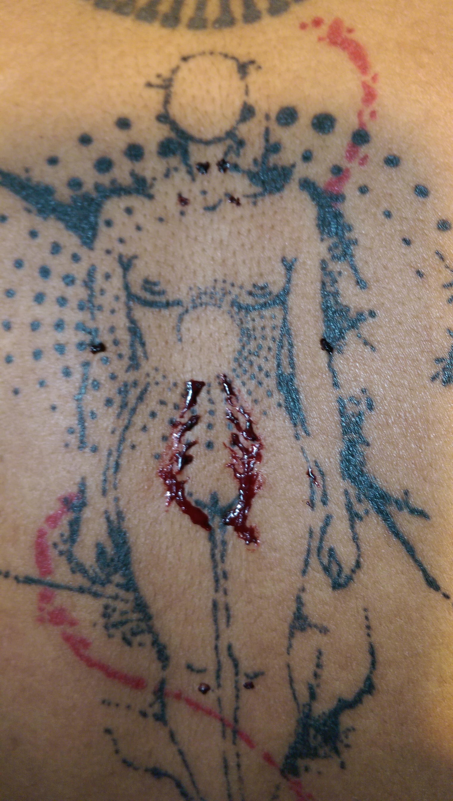 Black ink tattoo on brown skin: a nude front-facing woman in front of a dotted spiral and red accent swirl. Blood is painted on it.