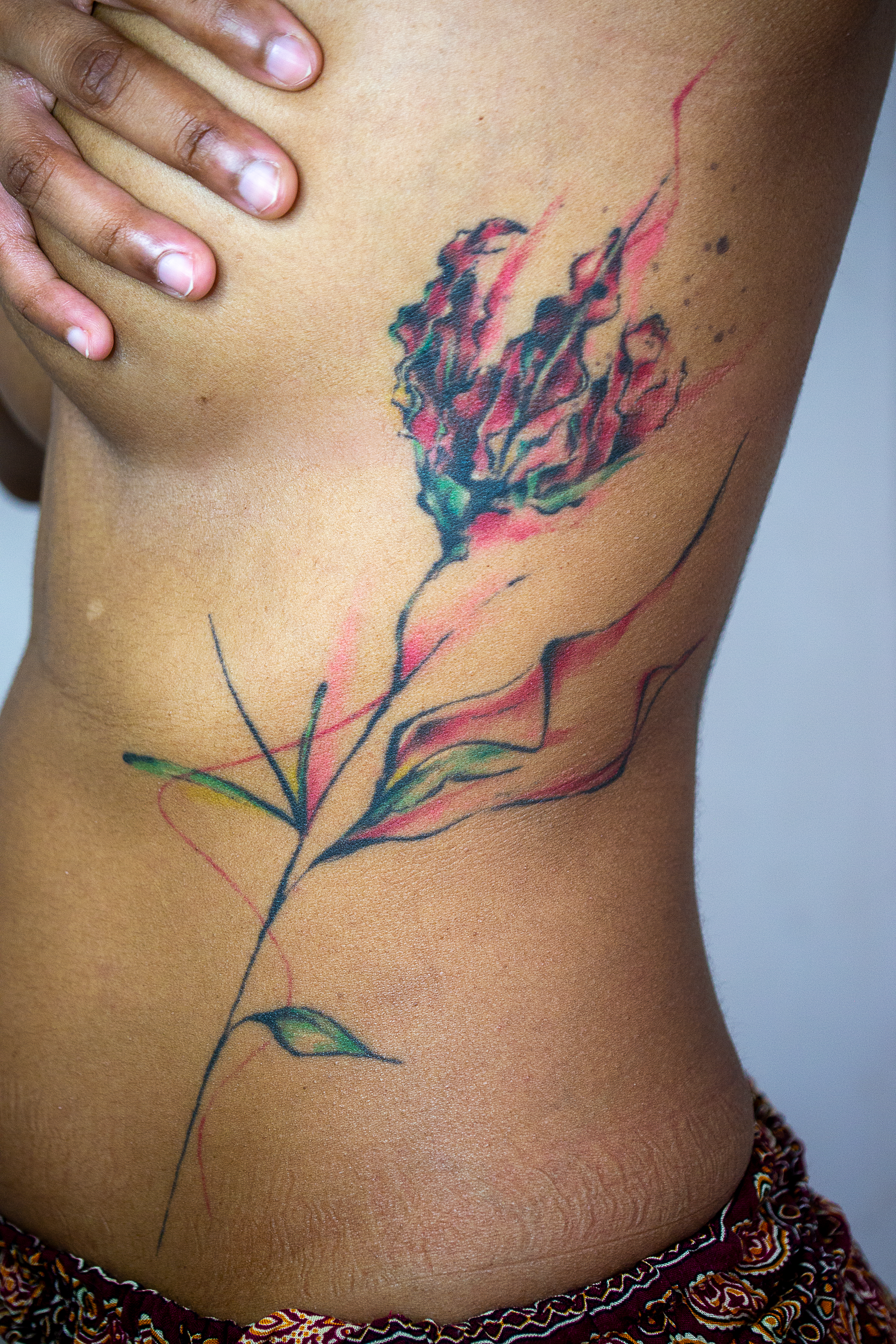 Watercolor rib tattoo of a flame lily on brown skin.