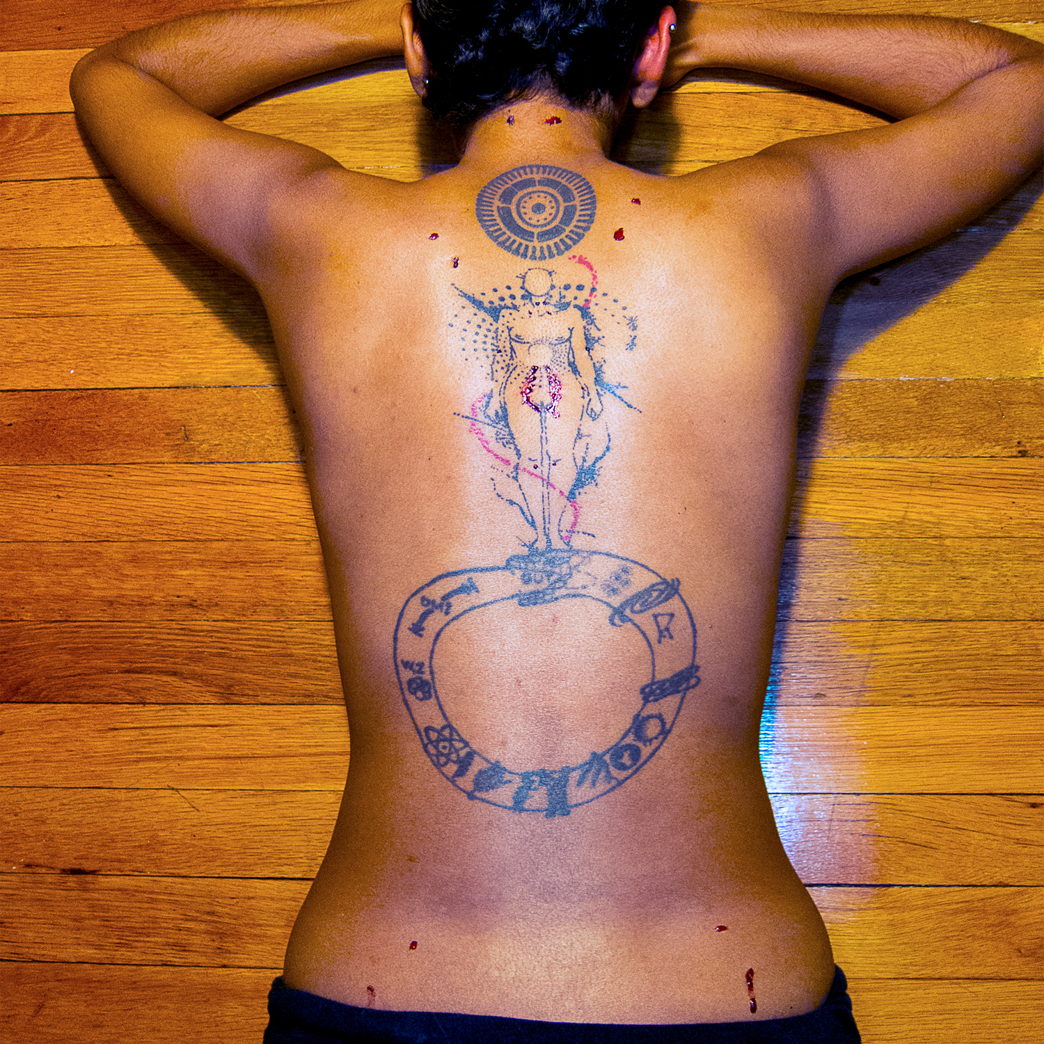 A Tamil woman's tattooed back, dotted with blood.
