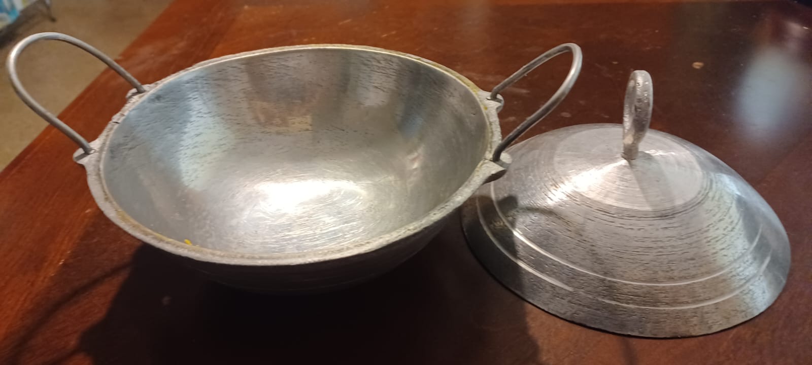 Without its lid, a small, grooved, silver aluminum appachatti displays the pot's rough, slightly tarnished rim and an interior inscribed with a record of immigration and culinary use.