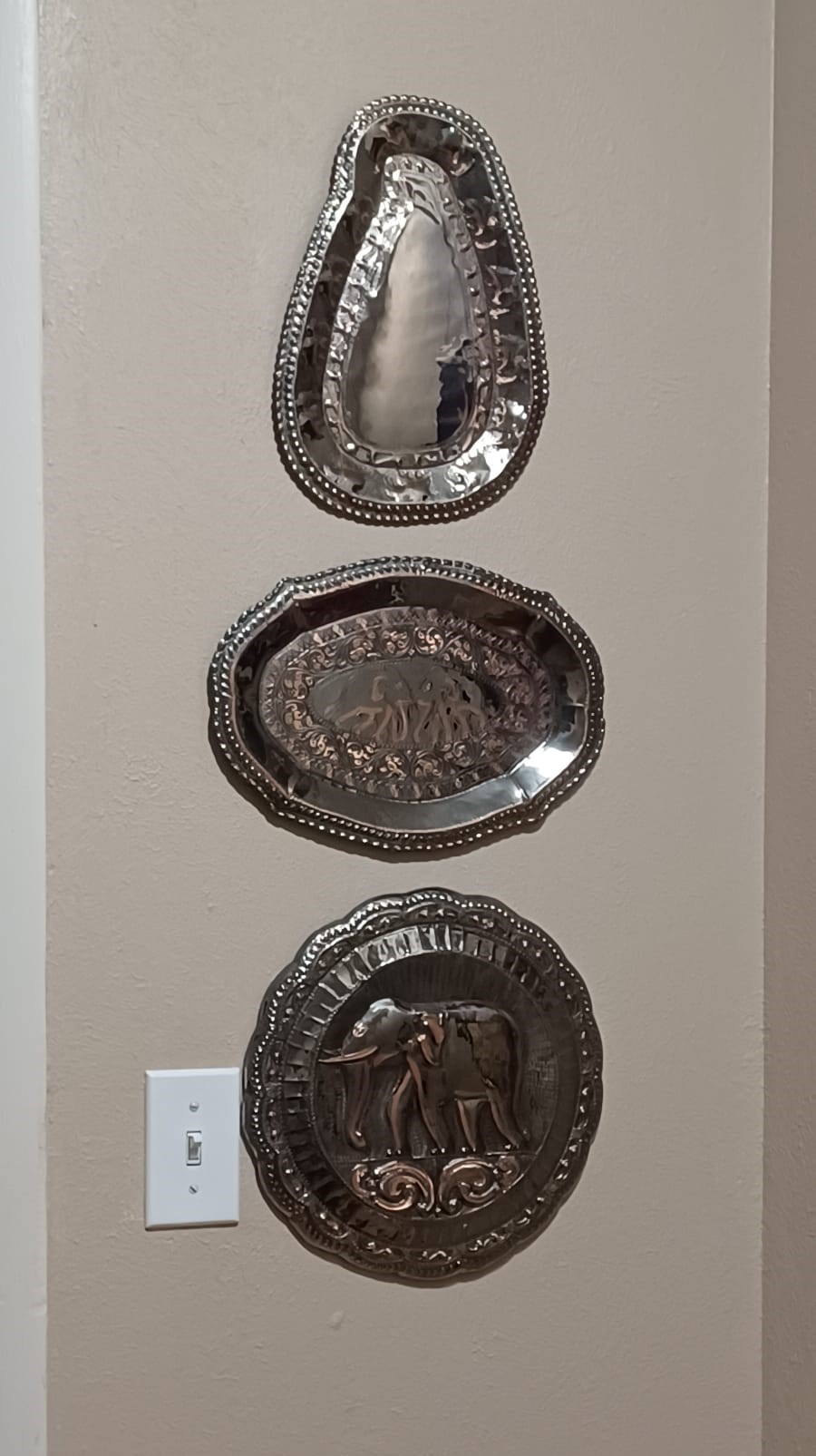 Three hammered brass plaques with scalloped, beaded edges and elephant motifs hang on a wall.