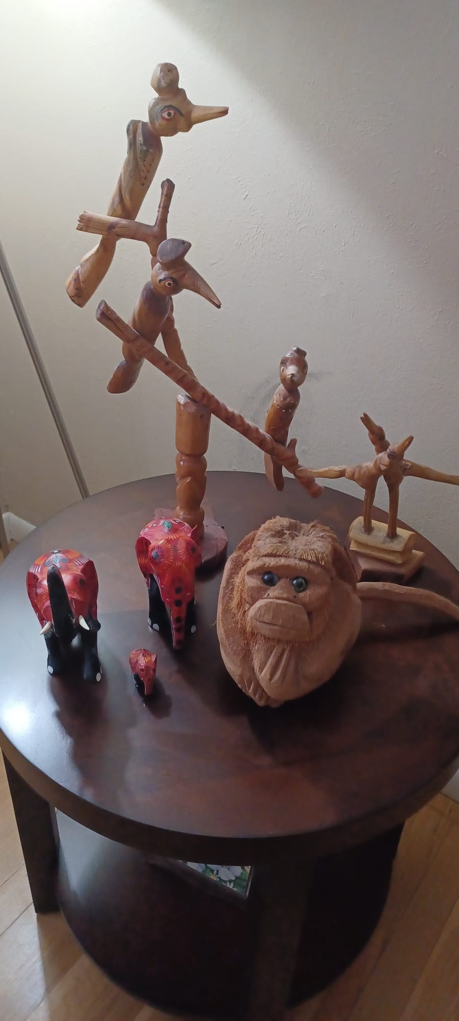 Traditional Sri Lankan handcrafts sit on a walnut table: wooden birds perched on crooked branches; a coconut husk monkey with glassy eyes and folded arms; and a family of wooden elephants painted red, black, and white.