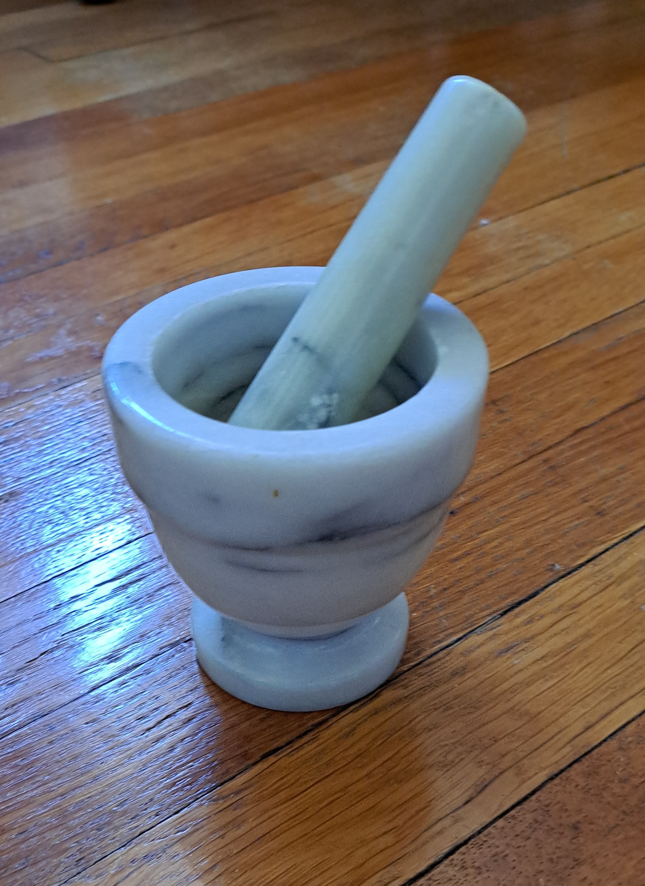 A small marble mortar and pestle sits on a hardwood floor.