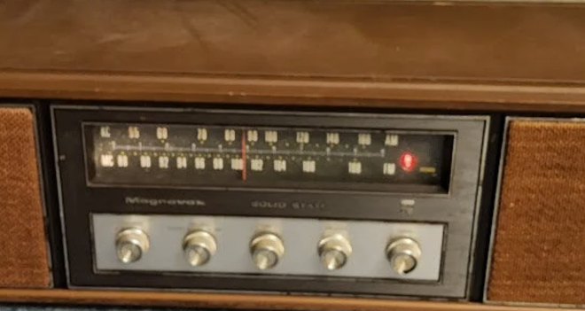 A vintage Magnavox Solid State radio with an AM/FM dial, five silver knobs, a walnut finish, and tan speakers.
