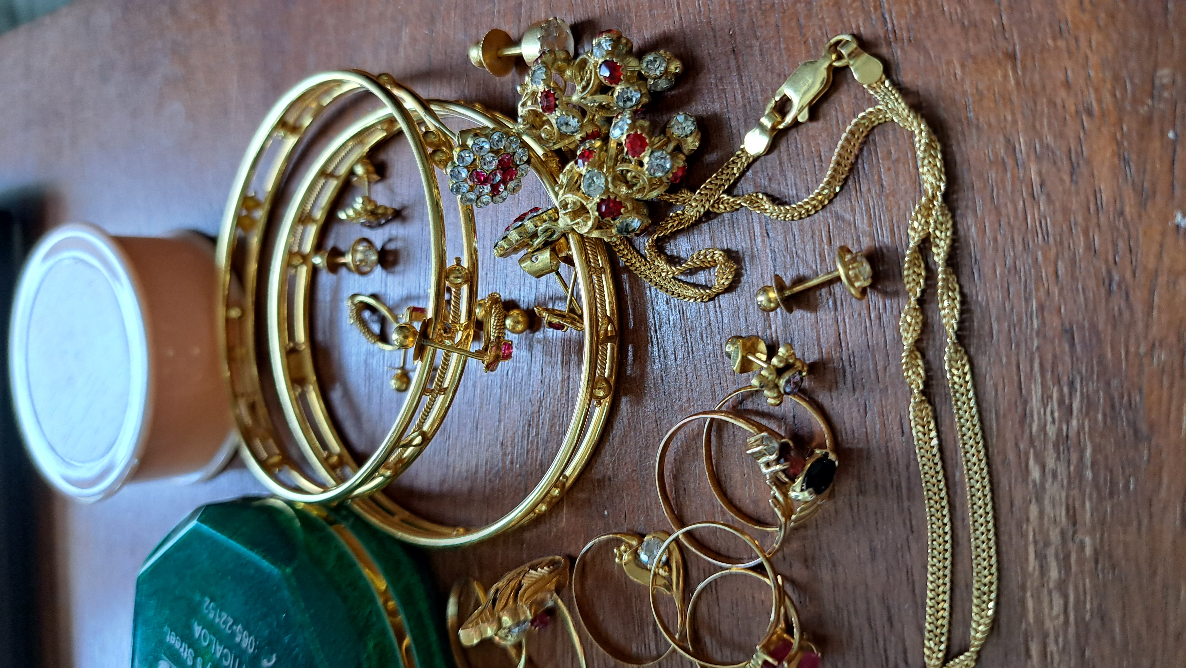 Gold bangles, earrings, and rings, some set with diamonds, semiprecious stones, or paste gems, sit on a walnut desk next to jewelry containers from Batticaloa.