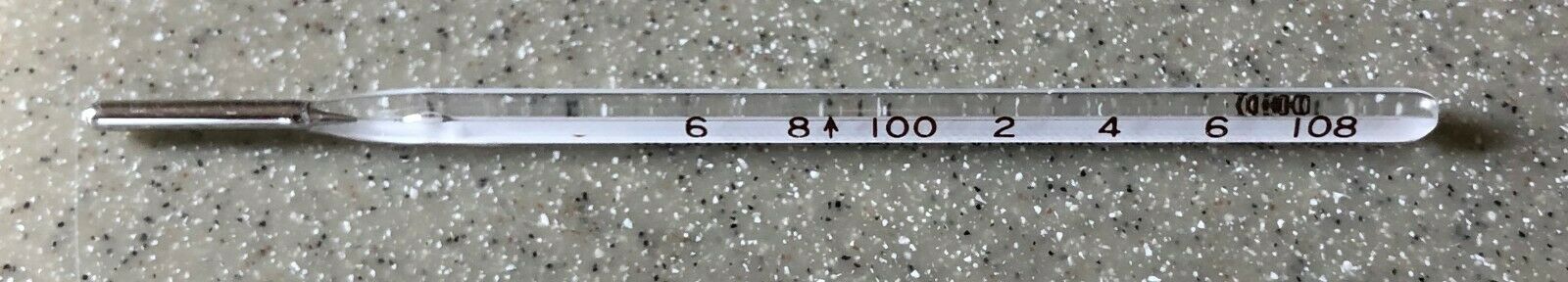 A glass mercury thermometer with a long silver tip, gradated from 6 to 108, sits on a granite counter.