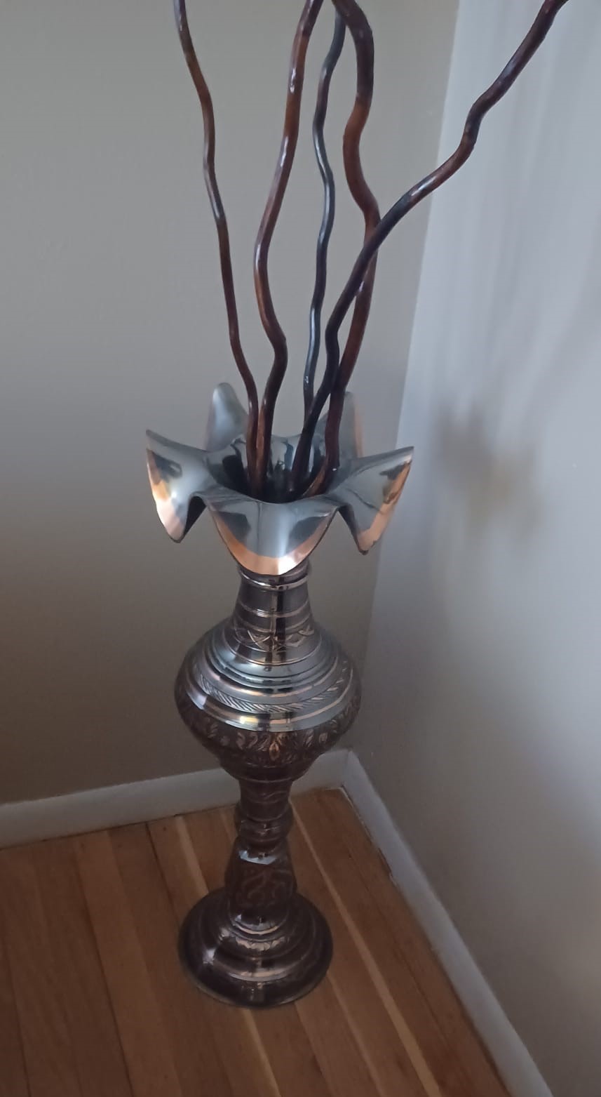 A brass vase with a flared lip, embossed and oxidized with patterns, holds five decorative willow branches.
